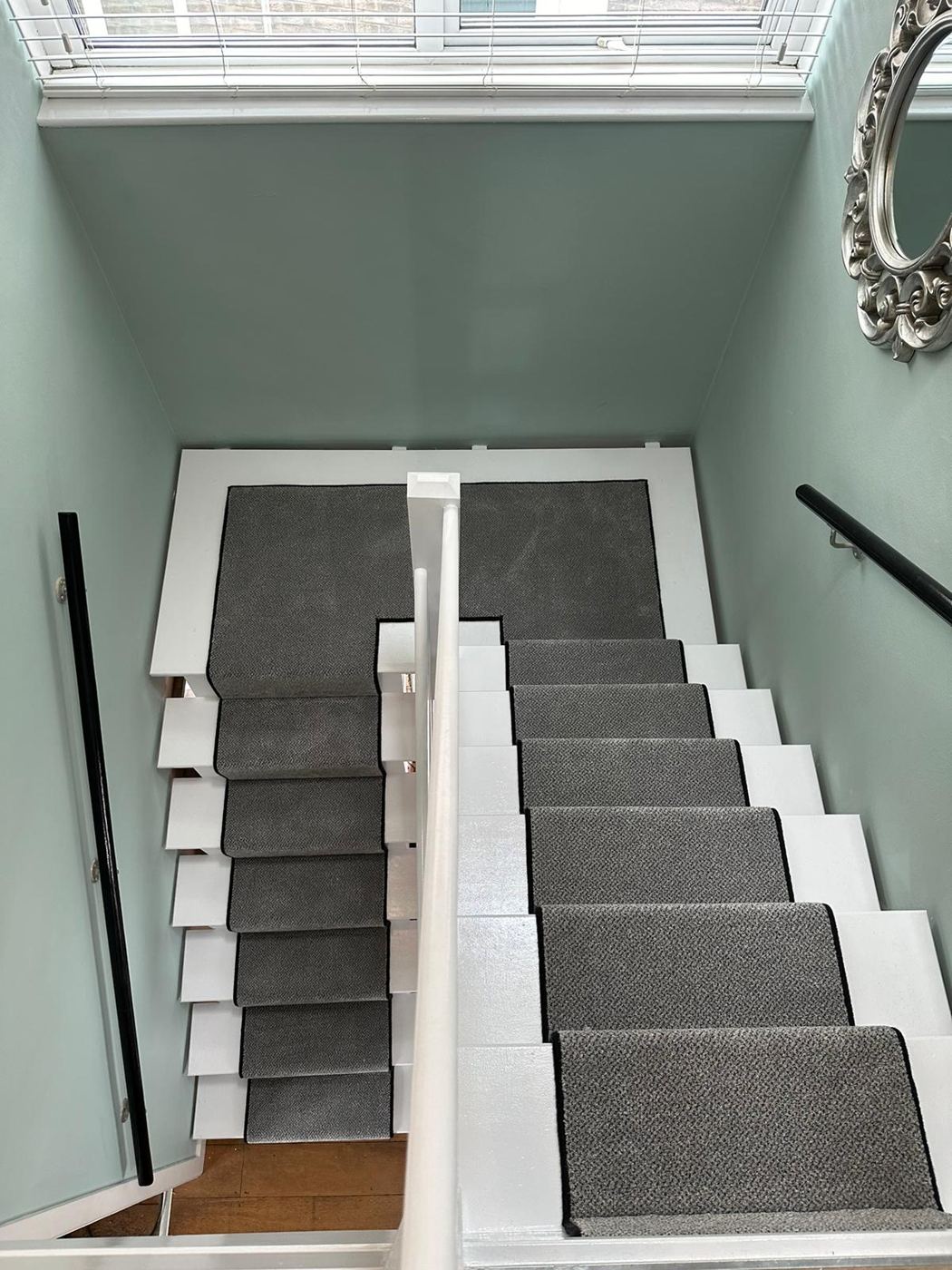 Grey runners on white stairs beside a sage green wall